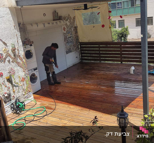 אדם מנקה דק עץ עם צינור מים בגינה